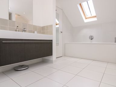 A bathroom with a bathtub under a skylight and a sink with a cabinet below at The Upper Deck in Porthcurno