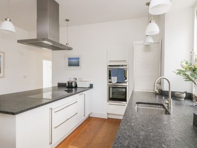 A kitchen with white cabinets dark countertops stainless steel appliances and wooden floor at The Upper Deck in Porthcurno