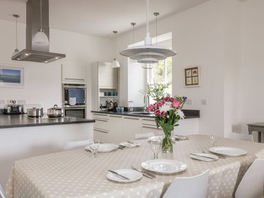 A kitchen with a dining table set with plates and glasses and a flower vase at The Upper Deck in Porthcurno