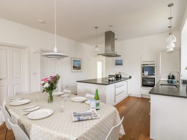 A kitchen with a dining table set with plates glasses and cutlery and a bouquet of flowers on a table at The Upper Deck in Porthcurno