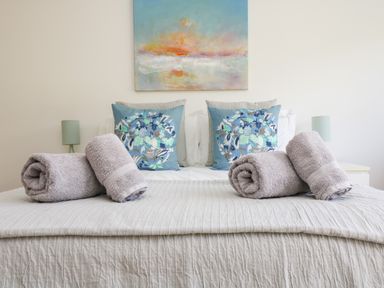 A bed with rolled towels and floral pillows under a painting at The Upper Deck in Porthcurno