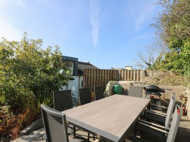 An outdoor patio with a dining table and chairs a barbecue and plants at The Upper Deck in Porthcurno