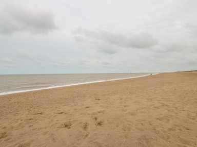 A sandy beach with a calm sea and cloudy sky at Moggs Retreat in Chapel St Leonards
