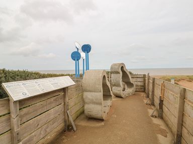 An outdoor wooden fenced area with two large cloud-shaped concrete structures and blue circular panels near the coast at Moggs Retreat in Chapel St Leonards