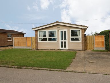 A small single-story house with a front lawn driveway and wooden fences at Moggs Retreat in Chapel St Leonards