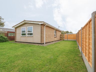 A single story house with brick and siding walls on a grass lawn with wooden fences and a garden shed at Moggs Retreat in Chapel St Leonards