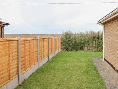 A backyard with a wooden fence a grassy lawn and a brick house at Moggs Retreat in Chapel St Leonards