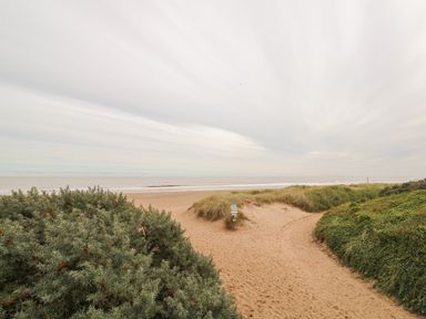 A sandy beach path leading to the sea with vegetation on both sides at Moggs Retreat in Chapel St Leonards