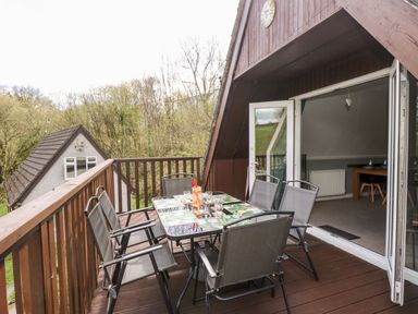 An outdoor balcony with a dining table and six chairs overlooking trees and a nearby building at Valley Lodge 52 in Callington