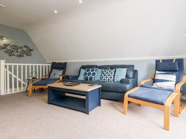 A living room with a blue leather sofa two blue armchairs a blue coffee table and a metal fish wall decoration at Valley Lodge 52 in Callington
