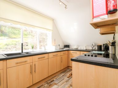 A kitchen with wooden cabinets a black countertop a window with a view of grass and trees at Valley Lodge 52 in Callington