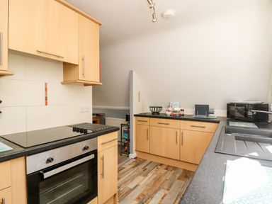 A kitchen with wooden cabinets a black countertop an oven a stove a sink a microwave and various items on the counter at Valley Lodge 52 Callington
