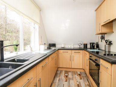 A kitchen with wooden cabinets black countertops a window with a blind and various appliances at Valley Lodge 52 in Callington