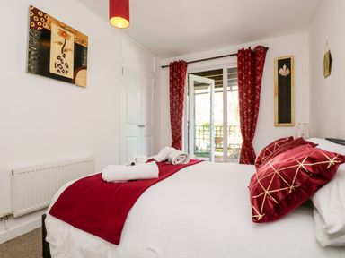 A bedroom with a bed red pillows and blanket white towels on the bed and glass doors with red curtains at Valley Lodge 52 Callington