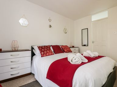 A bedroom with a bed with red pillows and a red throw with white towels on it and white cabinets on each side and a full length mirror on the wall at Valley Lodge 52 in Callington