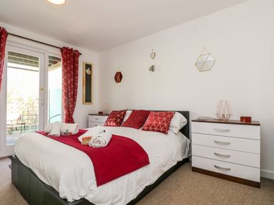 A bedroom with a bed with red cushions and a red throw a dresser and glass doors at Valley Lodge 52 Callington