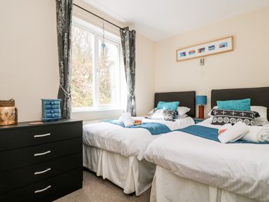 A bedroom with two single beds black chest of drawers and window with curtains at Valley Lodge 52 in Callington