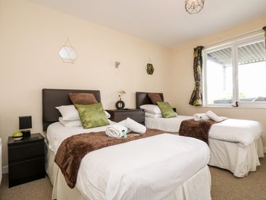 A bedroom with two single beds with brown and green pillows and white linens at Valley Lodge 52 in Callington