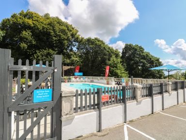 An outdoor swimming pool area surrounded by a black wooden fence and trees at Valley Lodge 52 in Callington