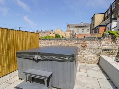 A covered hot tub with steps on a tiled patio surrounded by wooden fence and brick walls at Station House in Scarborough