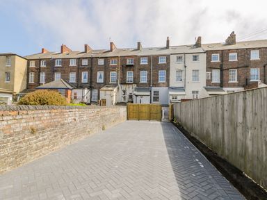 A paved driveway between a brick wall and wooden fence leading to a gate with terraced houses in the background at Station House in Scarborough