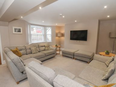 A living room with gray sofas, a wall-mounted TV, two ottomans, side tables with lamps, and a bay window at Station House in Scarborough