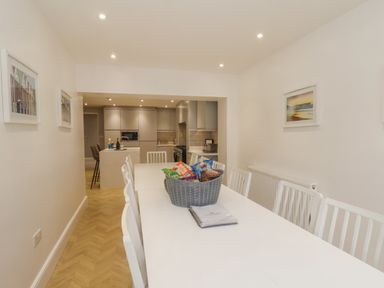 A dining room with white table and chairs leading to a kitchen with grey cabinets at Station House in Scarborough