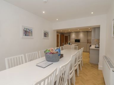 A dining room with a long white table and white chairs facing a kitchen at Station House in Scarborough
