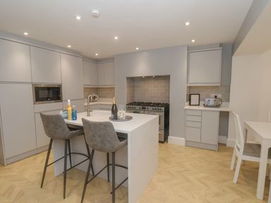 A kitchen with an island and two bar stools a gas stove microwave toaster and a small dining table at Station House in Scarborough