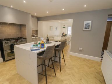 A kitchen with an island and bar stools leading to a dining area with a long table and chairs at Station House in Scarborough