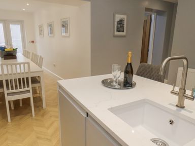 A kitchen island with a sink and faucet a bottle and glasses on a tray and a dining table with chairs in the background at Station House in Scarborough