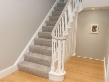 A staircase with carpeted steps and white banister in a hallway with wooden floor at Station House in Scarborough