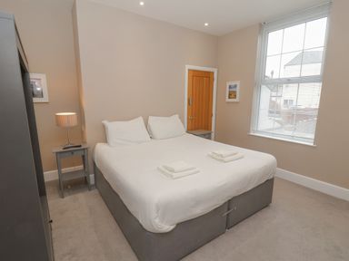A bedroom with a large bed with white linens and towels bedside tables with lamps a window and a wooden door at Station House in Scarborough