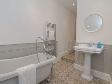 A bathroom with a freestanding bathtub a pedestal sink a round mirror and patterned floor tiles at Station House in Scarborough