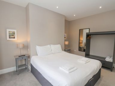 A bedroom with a double bed white linens bedside tables with lamps a large mirror and open wardrobe at Station House in Scarborough