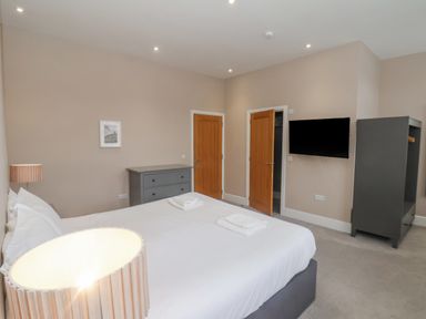 A bedroom with a bed a lamp a chest of drawers a wardrobe a wall-mounted television and two wooden doors at Station House in Scarborough