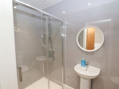 A bathroom with a glass shower enclosure a white sink with soap and a round mirror at Station House in Scarborough