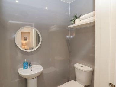 A bathroom with a pedestal sink holding soap a round mirror above it a toilet under a shelf with towels and a plant at Station House in Scarborough