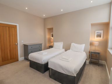A bedroom with two single beds a gray chest of drawers and two bedside tables with lamps at Station House in Scarborough