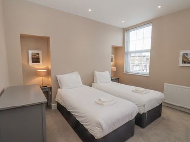 A bedroom with two single beds with white bedding two bedside tables with lamps a grey dresser and a window at Station House in Scarborough