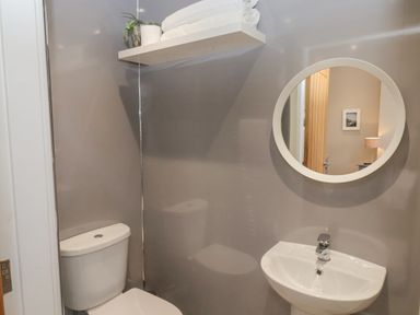 A bathroom with a toilet sink round mirror and a shelf with towels and a plant at Station House in Scarborough