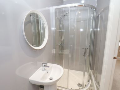 A bathroom with a pedestal sink a round mirror and a corner shower enclosure at Station House in Scarborough