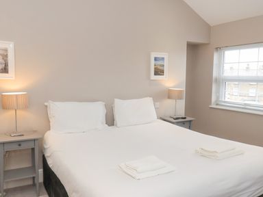 A bedroom with two single beds pushed together each with white bedding and towels on top bedside tables with lamps and framed pictures on walls at Station House in Scarborough