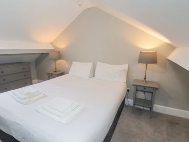 A bedroom with a double bed white linens two bedside tables with lamps and a chest of drawers at Station House in Scarborough