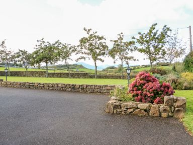A paved driveway with a stone flower bed containing pink flowers and a row of small trees behind a stone wall at The Blue Annex in The Spa near Tralee County Kerry