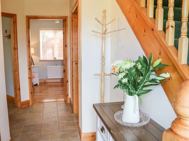 An entryway with a wooden coat rack a vase with flowers on a table and stairs with wooden handrail at The Blue Annex The Spa near Tralee County Kerry