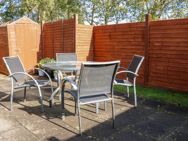 An outdoor patio with a round glass table surrounded by four metal chairs next to a wooden shed and fenced garden at The Blue Annex in The Spa near Tralee County Kerry