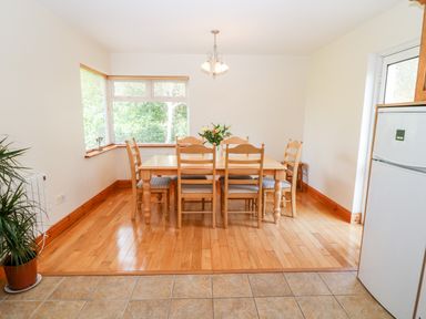 A dining area with a wooden table and six chairs under a ceiling light near a window with blinds and a refrigerator at The Blue Annex in The Spa near Tralee County Kerry