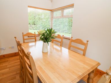 A dining room with a wooden table and six chairs and a vase with flowers on the table at The Blue Annex The Spa near Tralee County Kerry