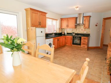 A kitchen with wooden cabinets a refrigerator a washing machine a stove and a wooden table with chairs and a vase of flowers at The Blue Annex in The Spa near Tralee County Kerry